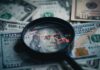 America’s Next Economic Test Looms Magnifying glass over US dollar bills with stock market data displayed