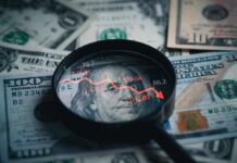 Magnifying glass over US dollar bills with stock market data displayed