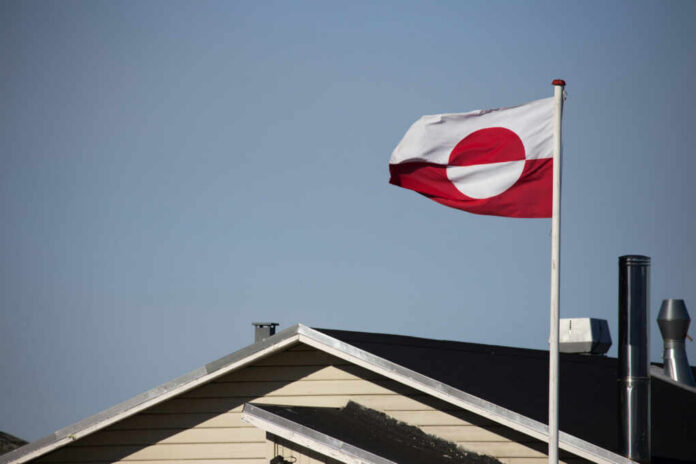 shutterstock_2558726337 Flag of Greenland waving in the wind above a house