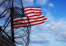 American flag waving near barbed wire against a blue sky