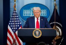 A political figure at a podium during a press conference in front of the White House