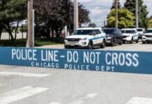 Yellow police caution tape at a crime scene with blurred figures in the background
