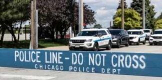 Crowd Ambushed—City Demands Accountability Yellow police caution tape at a crime scene with blurred figures in the background