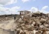 Person walking past rubble and destroyed buildings on a dirt road