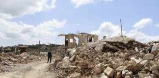 Person walking past rubble and destroyed buildings on a dirt road