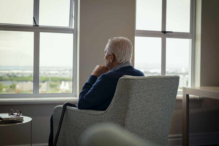 shutterstock1977447137jpg Elderly man sitting in a chair, looking out a window with a thoughtful expression