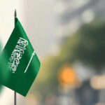 Deadly Crash Rocks Saudi Oil Hub A green flag of Saudi Arabia with white Arabic text and a sword, set against a blurred background