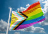 Rainbow Branding Backfires — Hypocrisy Exposed A colorful pride flag waving against a blue sky with clouds