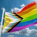 A colorful pride flag waving against a blue sky with clouds