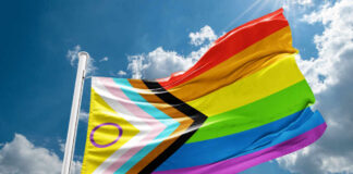A colorful pride flag waving against a blue sky with clouds