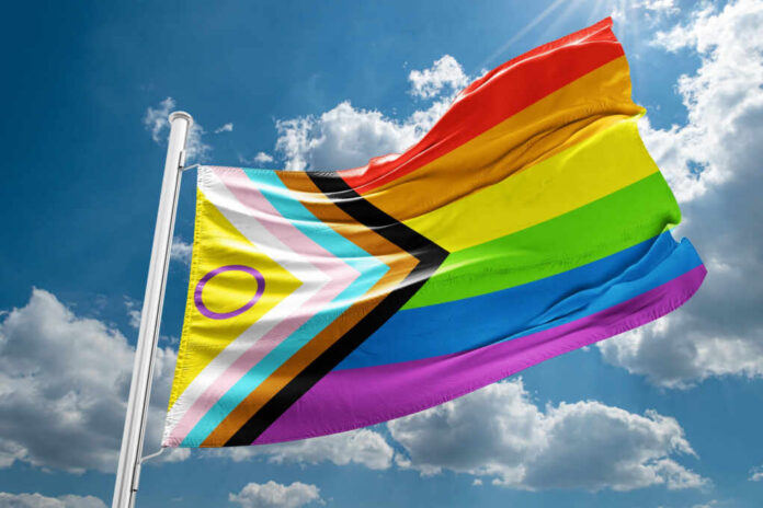 shutterstock2474415413jpg A colorful pride flag waving against a blue sky with clouds