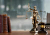Federal Judge Charged After Parking Lot Meltdown A bronze statue of Lady Justice holding scales and a sword, with law books and a gavel in the foreground