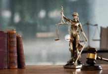 A bronze statue of Lady Justice holding scales and a sword, with law books and a gavel in the foreground