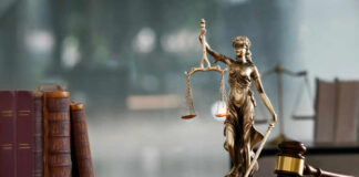 A bronze statue of Lady Justice holding scales and a sword, with law books and a gavel in the foreground