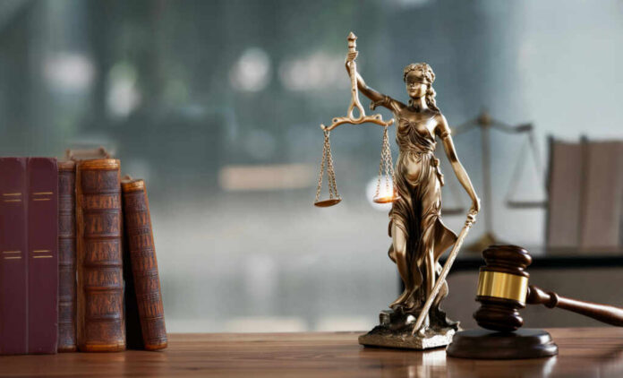 A bronze statue of Lady Justice holding scales and a sword, with law books and a gavel in the foreground