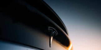 Close-up of a Tesla logo on a black car with a sunset in the background
