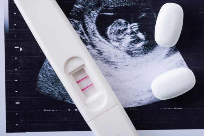 Close,Up,Of,Pills,And,Pregnancy,Test,On,Ultrasound,Image Pregnancy test next to an ultrasound image and two white tablets