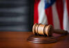 Light Rail Killing — Justice Stuck Again? A wooden gavel resting on a round base with a blurred American flag in the background