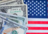 Various denominations of US dollar bills on an American flag background