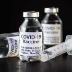 Vials of COVID-19 vaccine and a syringe on a dark background