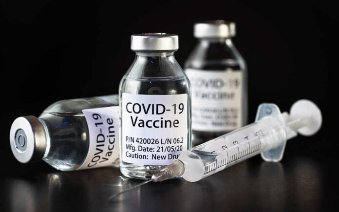 Vials of COVID-19 vaccine and a syringe on a dark background