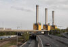 Industrial power plant with three tall smokestacks beside a highway
