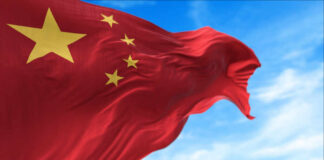 Waving Chinese flag with five yellow stars against a blue sky