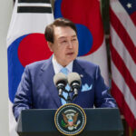 A government official delivering a speech at a podium with flags in the background