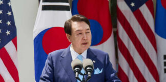 A government official delivering a speech at a podium with flags in the background