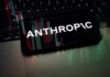 Jailbreak Panic Triggers Global AI Blackout Mobile phone displaying the word 'ANTHROPIC' over a background of financial graphs