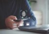 Person holding smartphone with fingerprint authentication near laptop
