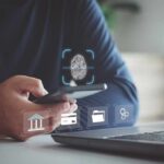 Person holding smartphone with fingerprint authentication near laptop
