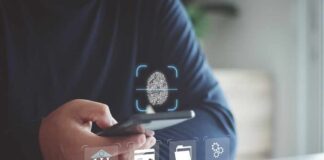 AI Layoffs Explode Across Big Banks Person holding smartphone with fingerprint authentication near laptop