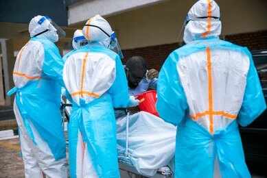 Medical workers in PPE assist a patient on a stretcher outdoors