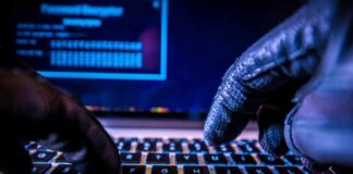 Close-up of gloved hands typing on a laptop keyboard in a dark setting