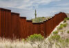 A rusty border wall in a desert landscape with a cactus in the background
