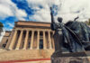 Bronze seated statue before a neoclassical building with tall columns