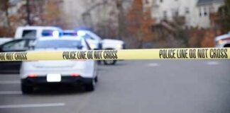 Police tape cordons off a street with patrol cars in the background