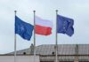 Flags of Finland and NATO waving in the wind against a clear blue sky