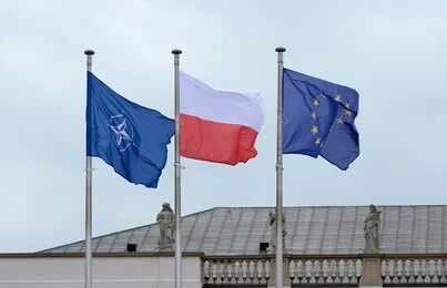 Flags of Finland and NATO waving in the wind against a clear blue sky