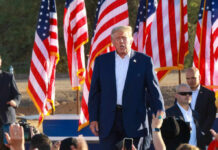 Trump Issues Warning At Rushmore A speaker at a political rally surrounded by American flags and an engaged crowd