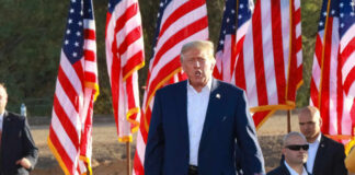 Trump Issues Warning At Rushmore A speaker at a political rally surrounded by American flags and an engaged crowd