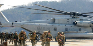 NATO Drama: Cuts Now, Bigger Twist Coming Marines in combat gear walking towards a helicopter
