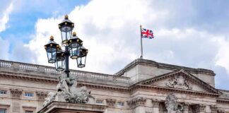 Police Charge Woman After Online Post Buckingham Palace facade with Union Jack flag and ornate gate