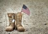 VA Enrollment Surges Under New Rules Combat boots with dog tags and a small American flag on gravel