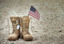 VA Enrollment Surges Under New Rules Combat boots with dog tags and a small American flag on gravel