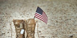Combat boots with dog tags and a small American flag on gravel