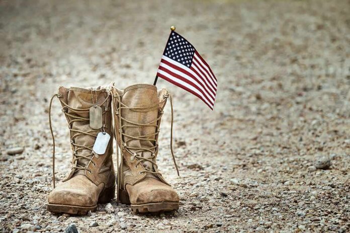 Combat boots with dog tags and a small American flag on gravel