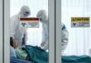 Healthcare workers in hazmat suits treat a patient in a quarantine room