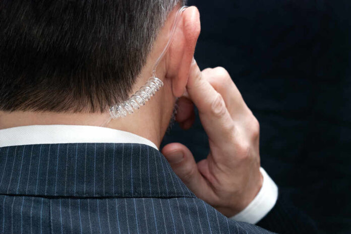 Close-up,Of,A,Secret,Service,Agent,Listening,To,His,Earpiece, Close-up of a man in a suit with an earpiece, indicating a security role